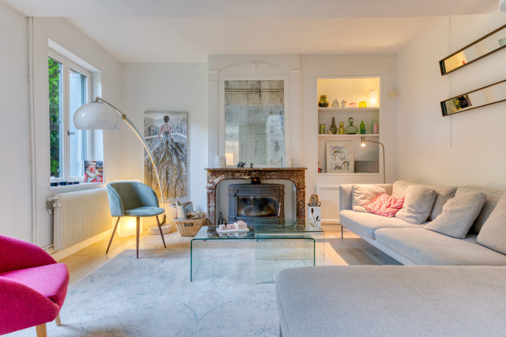 Intérieur moderne et cosy d'une maison. Les murs et mobiliers sont blancs. Il y a une cheminée au fond de la pièce.