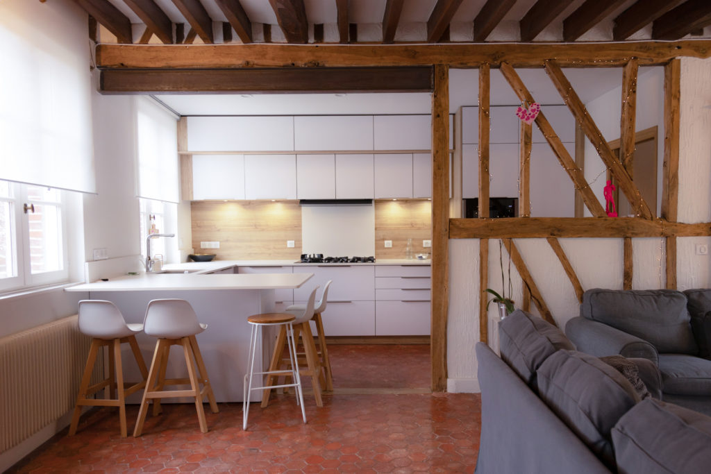 Intérieur d'une maison. Les murs sont blancs avec des poutres apparentes. Le mobilier est blanc et gris.