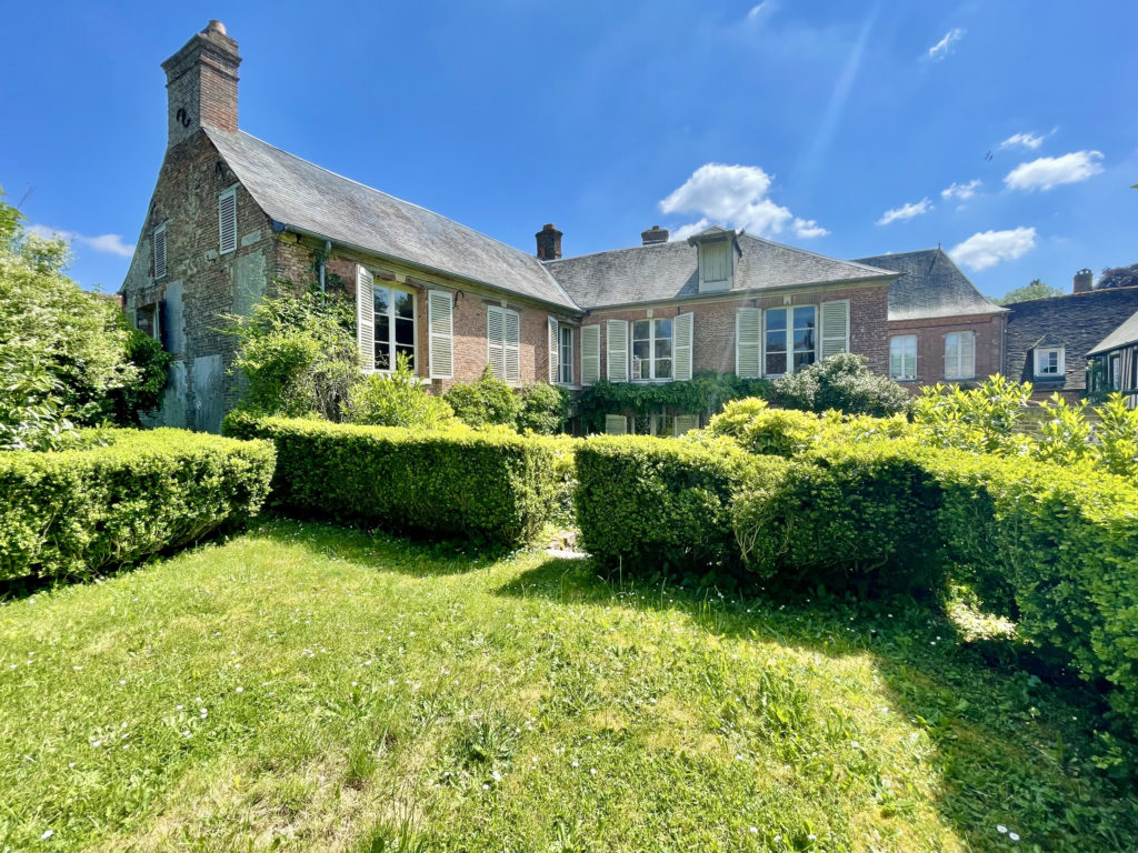 Vue extérieure d'une grande maison en brique. Celle-ci se trouve dans un jardin.